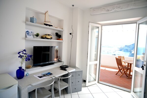 Une chambre moderne équipée d’un bureau, d’une télévision et offrant une vue sur la plage grâce à une porte vitrée.