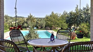 Eine Terrasse mit Korbstühlen und einem Tisch, mit Blick auf einen Swimmingpool und üppiges Grün.