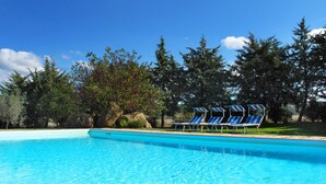 Ein klares, blaues Schwimmbecken mit Liegestühlen und Blick auf Bäume und Felsen.