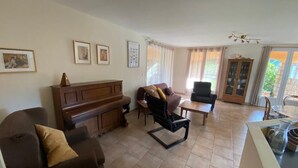 Tilava olohuone, jossa on piano, sohvia sekä ruokailutila pöytineen ja tuoleineen.