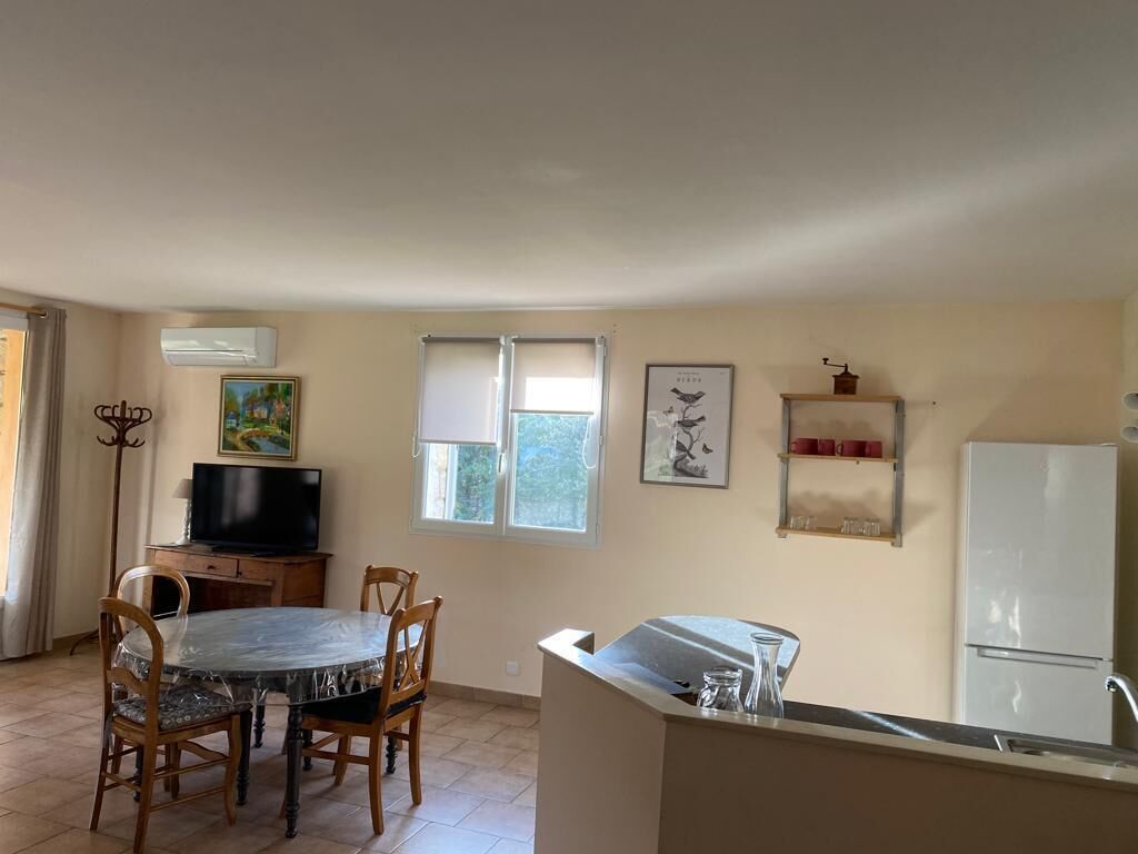 Une cuisine compacte comprenant une table à manger, des chaises, un réfrigérateur et un téléviseur.