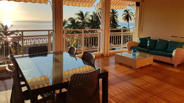 A spacious balcony with a view of the ocean, furnished with a table and chairs, and a sofa.