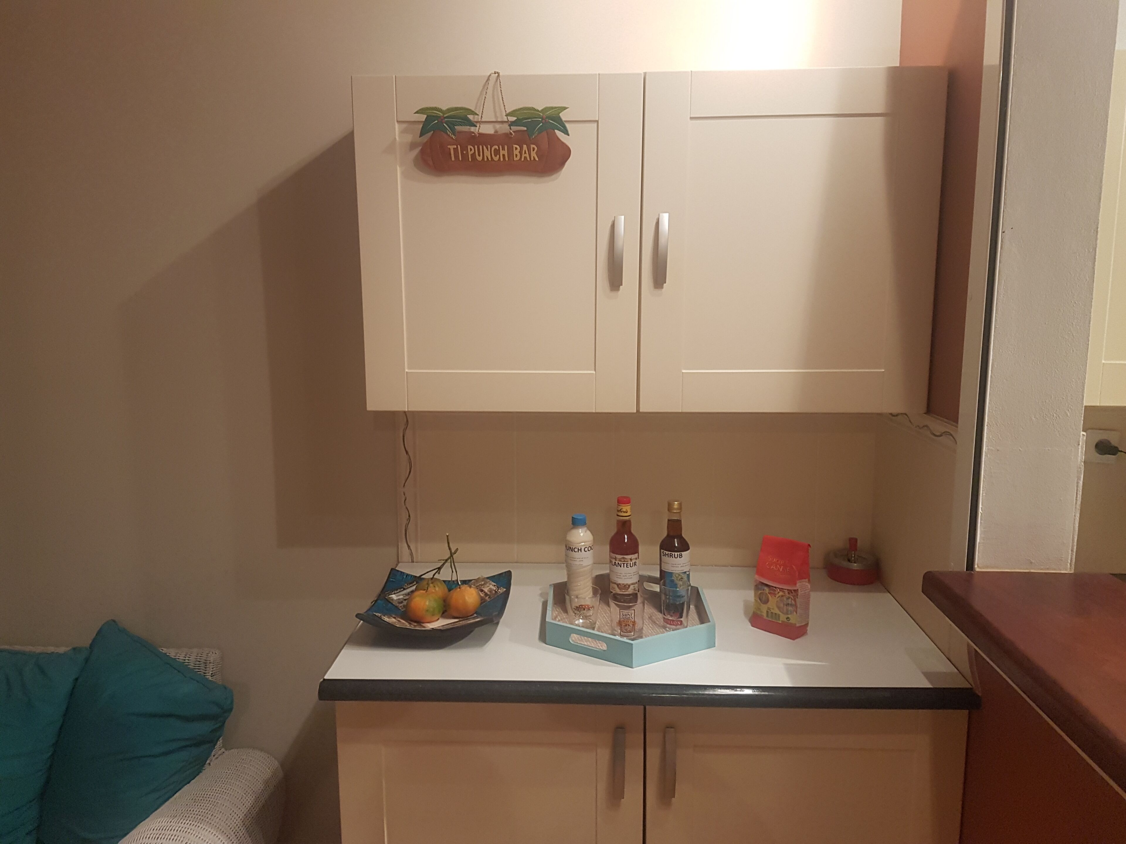 A kitchenette with a Ti-Punch Bar sign, a bowl of fruit, and condiments on the counter.