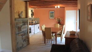 Un accogliente soggiorno con un divano in pelle marrone, una zona pranzo con tavolo e sedie in legno, e una cucina con parete in pietra ed elettrodomestici moderni.