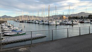 En lysthavn med mange både i havnen, en stenvæg og et bjerg i baggrunden.