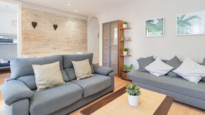 Een moderne woonkamer met twee grijze banken, een houten salontafel en een accentmuur van baksteen.