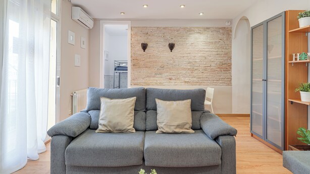 Een moderne woonkamer met een grijze bank, een bakstenen muur en een houten kast.