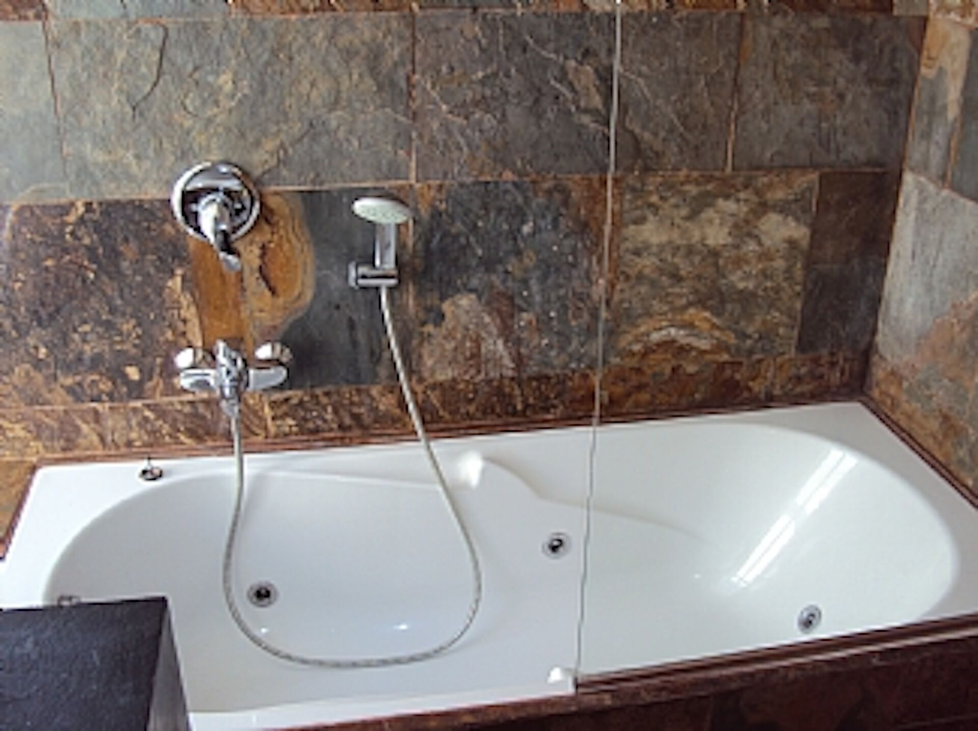 A bathtub with a shower head and faucet, set against a stone wall.