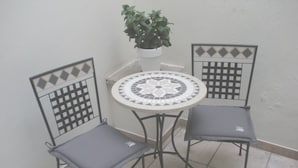 Un petit espace patio avec une table ronde et deux chaises, un pot de fleurs et un motif décoratif en carreaux sur le mur.