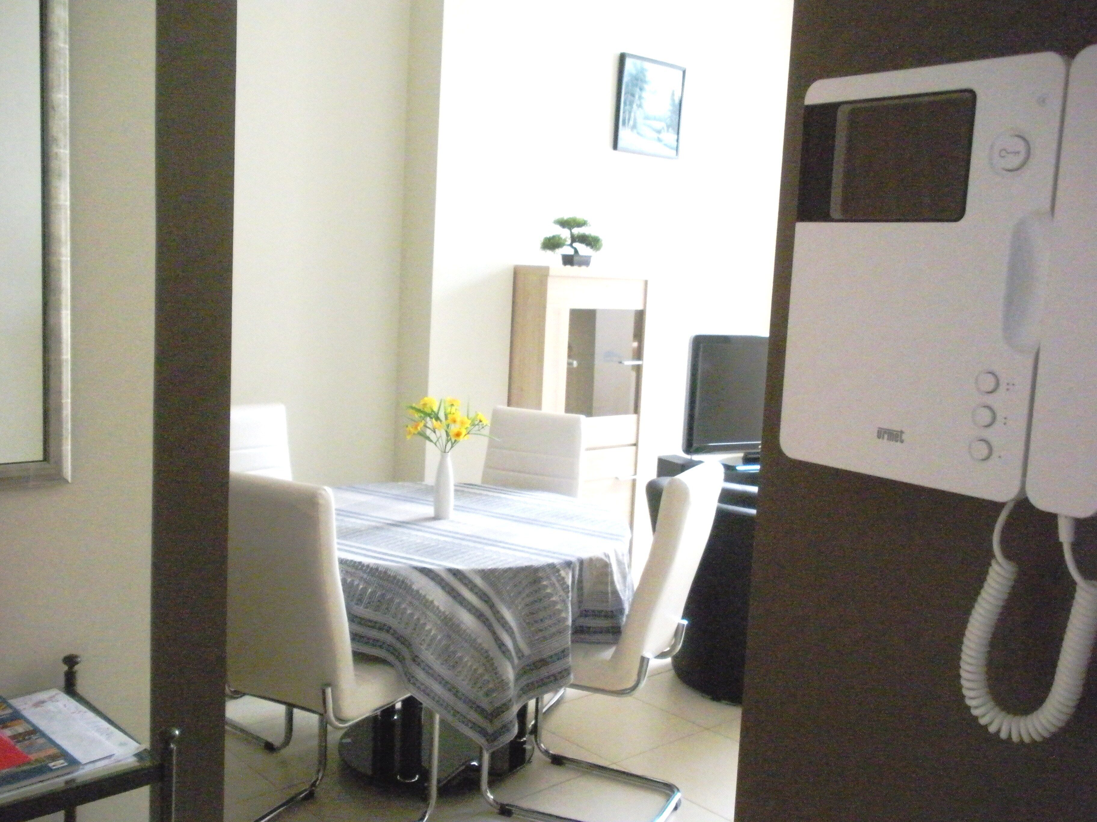 A dining area with a table, chairs, a vase with flowers, a cabinet, and a telephone.