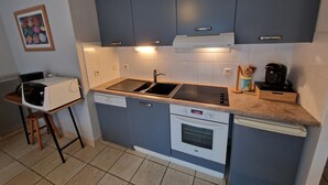 A compact kitchen with dark blue cabinets, a white dishwasher, a built-in oven, a microwave, a sink, and a coffee maker. - Apartment La Mouette Rated 3* (Saint-Philibert)