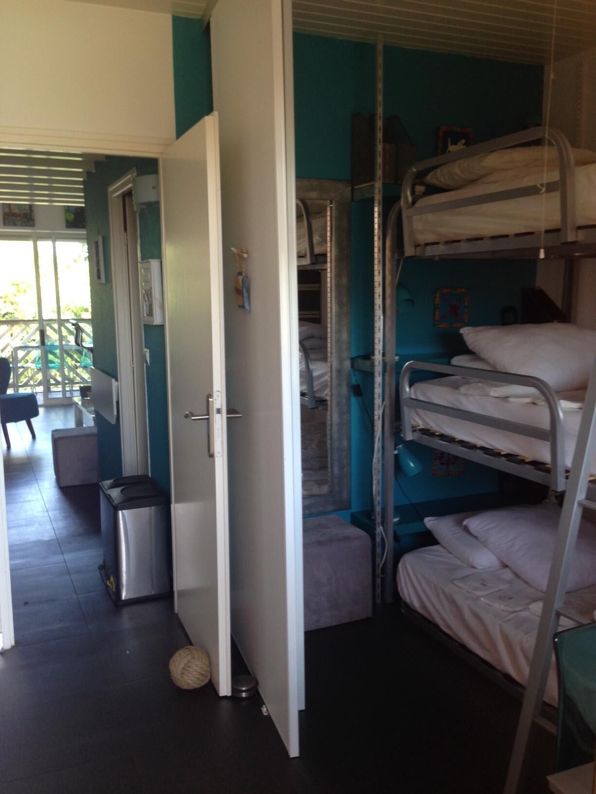 A dormitory room with bunk beds, a trash bin, and a door leading to a balcony.