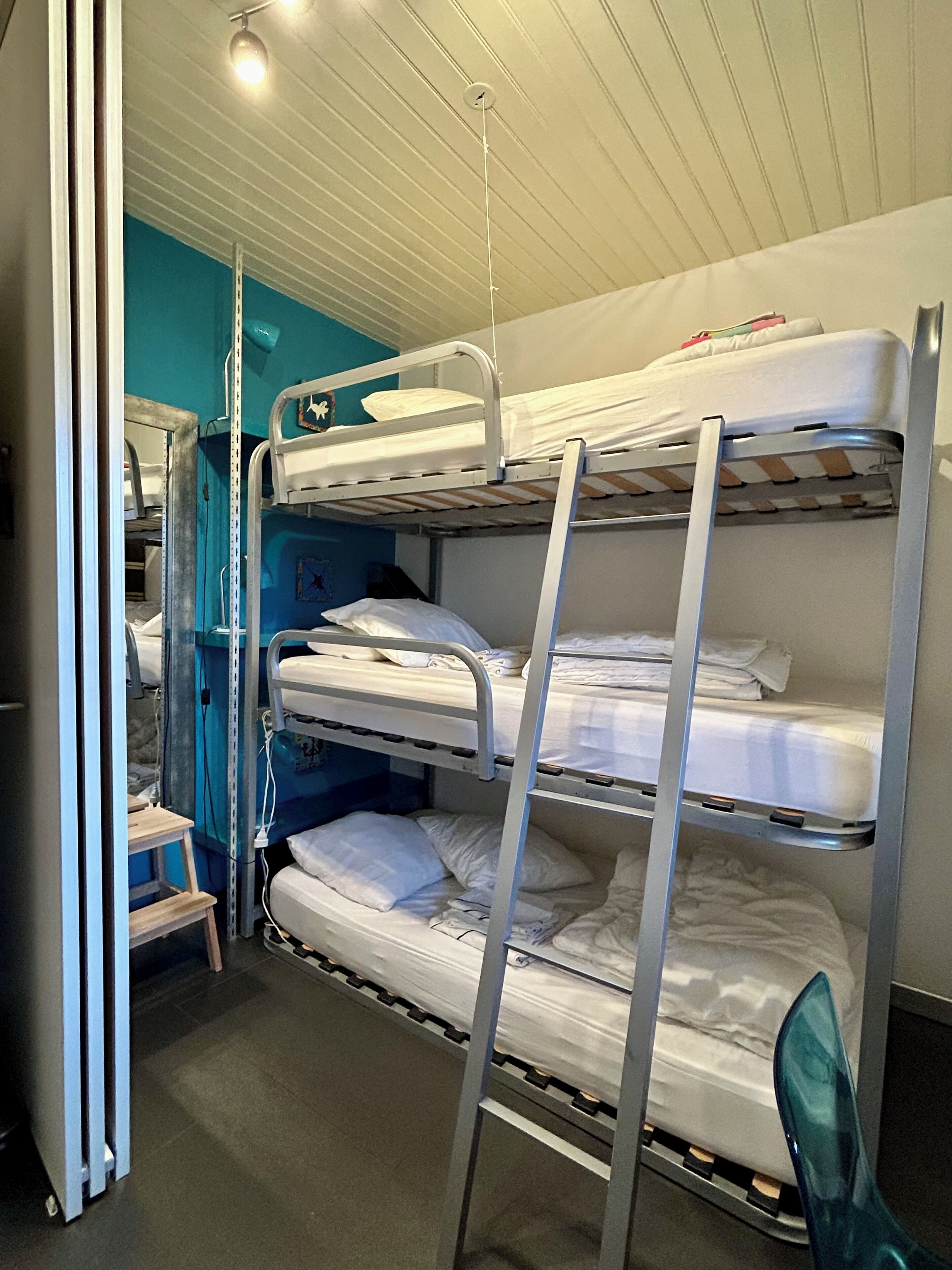 Une chambre avec un lit superposé, un mur bleu, un petit escabeau et un luminaire blanc au plafond.