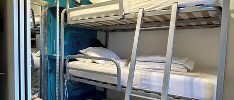 Une chambre avec un lit superposé, un mur bleu, un petit escabeau et un luminaire blanc au plafond.