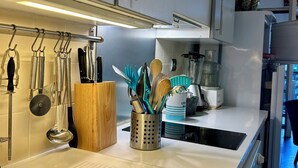 A modern kitchen with white cabinets, stainless steel appliances, and a variety of utensils and cookware.