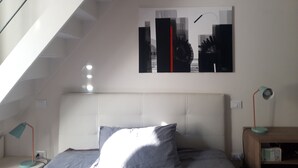 A bedroom with a sloped ceiling, a bed with grey bedding, a headboard, a wall-mounted artwork, and two bedside lamps.