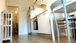 A modern kitchen with white cabinetry, a built-in oven, and a dining area with a wooden table and chairs.