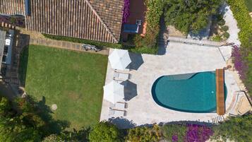 Vista aérea de una propiedad residencial con piscina, muebles de patio y césped.