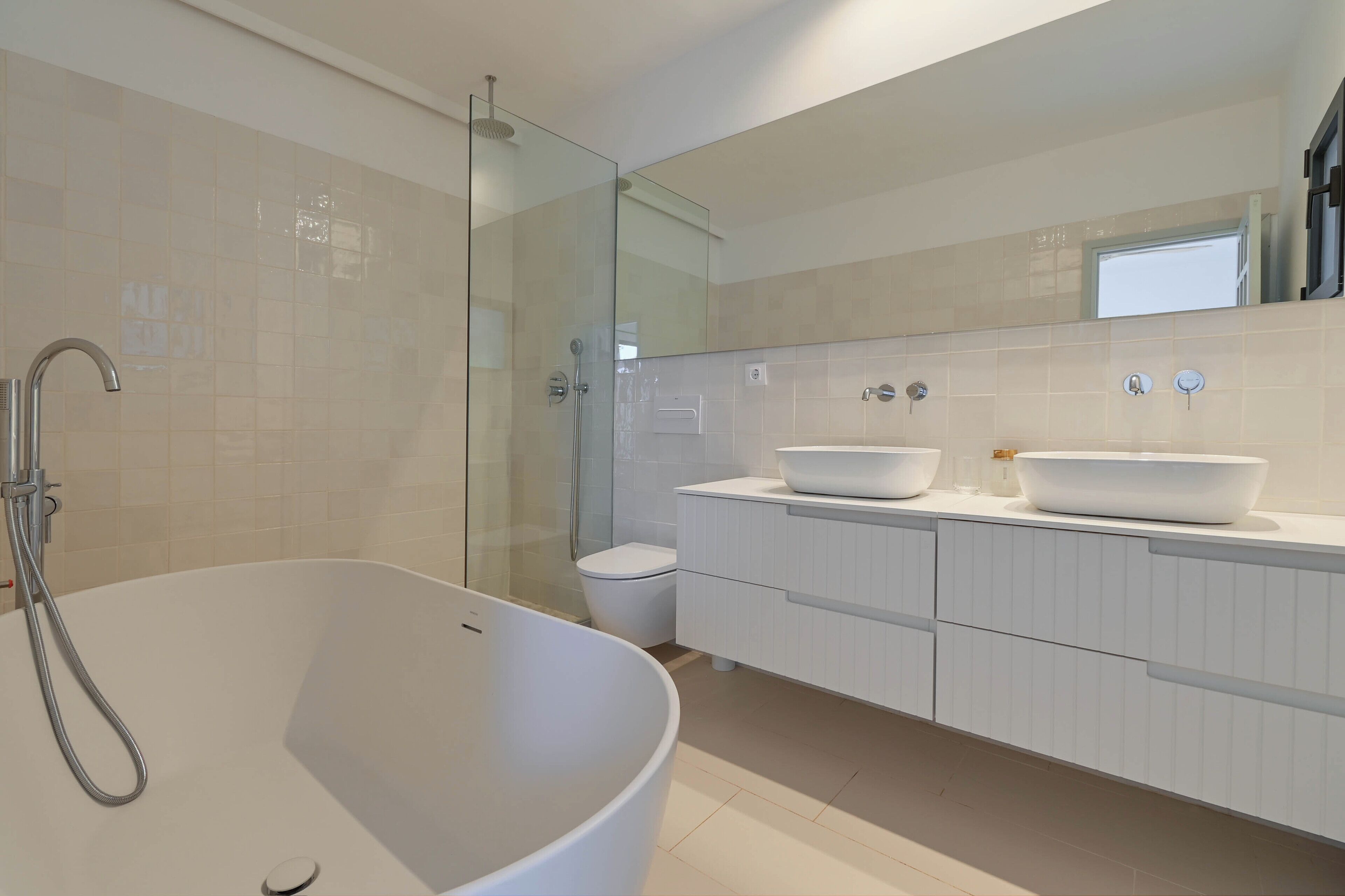 Un baño moderno con una bañera independiente, una ducha con mampara de cristal y un tocador blanco con dos lavamanos.