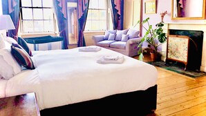 A bedroom with a large bed, a sofa, a small table, and a potted plant.