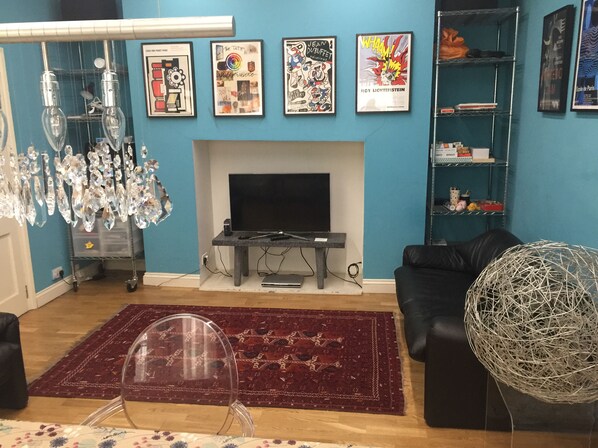 Ein Wohnzimmer mit Kamin, Fernseher, einer schwarzen Couch, einem roten Teppich und einer dekorativen Glaskugel.