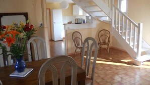 A dining area with a wooden table, chairs, and a vase of flowers. There is a staircase leading to an upper level.