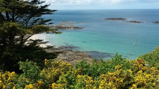 A coastal landscape with rocky shores, clear turquoise waters, and dense greenery.