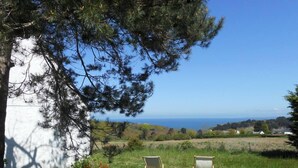 A grassy area with two wooden chairs facing a scenic view of the sea and distant houses.