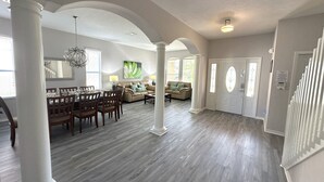 A spacious living area with a dining table, sofas, and a staircase.