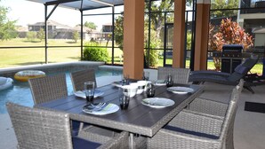 An outdoor dining area with a pool view, wicker furniture, and a barbecue grill.