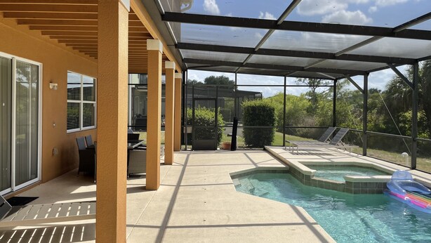 A covered outdoor pool area with a glass enclosure, lounge chairs, and a hot tub.