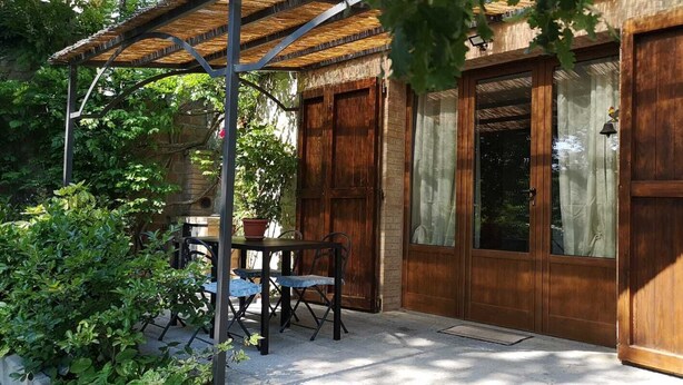Une terrasse avec une table et des chaises, une porte en bois et une fenêtre avec des rideaux.