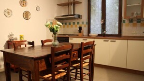 Une cuisine avec une table à manger en bois, des chaises, un vase de fleurs et une fenêtre avec des rideaux.