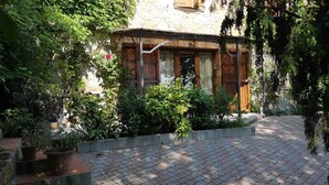 Un bâtiment rustique en bois, doté d’un toit en tuiles, entouré d’une végétation luxuriante et agrémenté de plantes en pot.