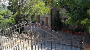 Un portail en fer forgé mène à une cour intérieure bordée de murs en pierre et agrémentée de plantes en pot.