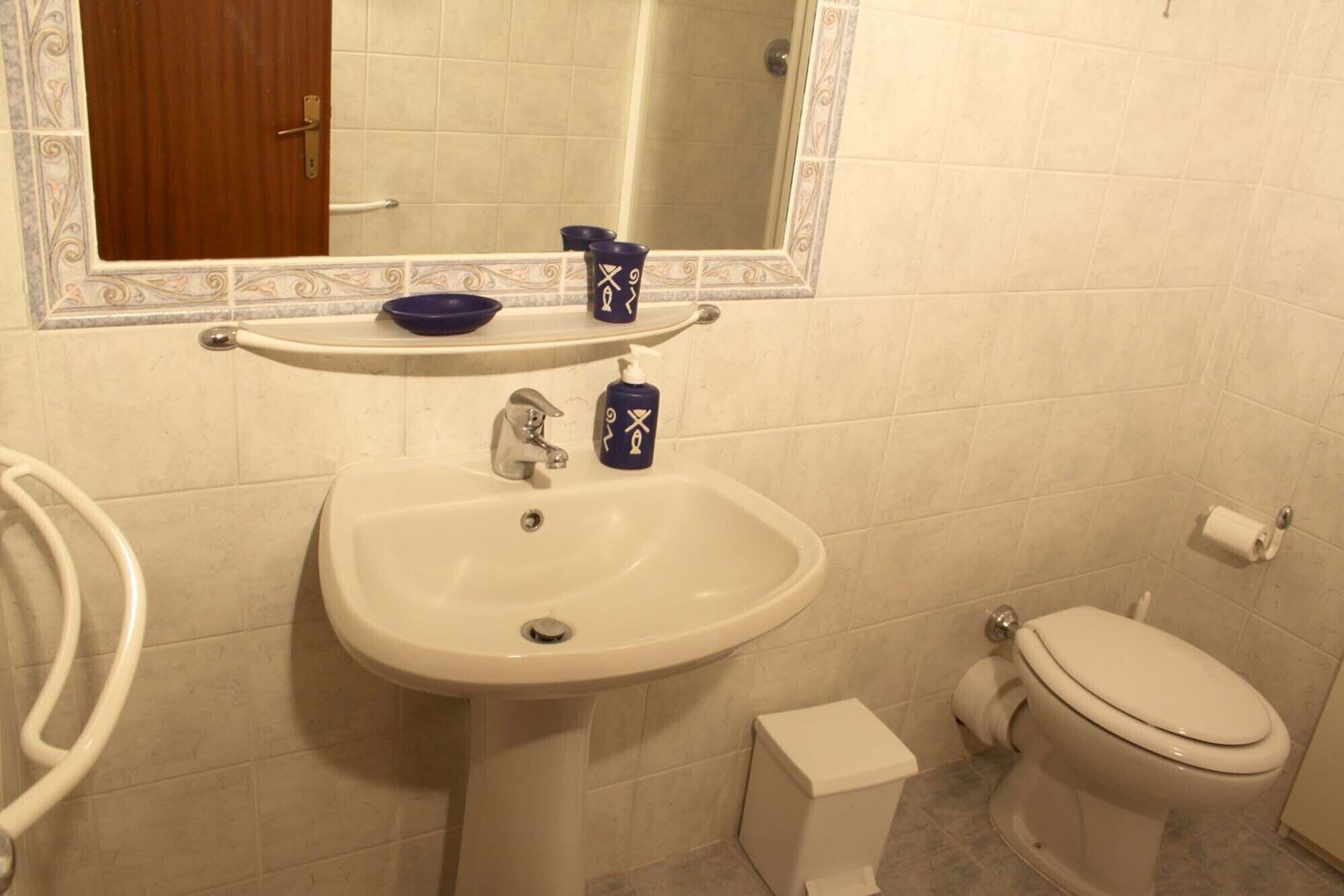 Ein Badezimmer mit weißem Waschbecken, einem Spiegel, einer Toilette und einem kleinen weißen Schrank.