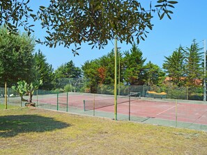 A tennis court with a net, surrounded by trees and a fence.