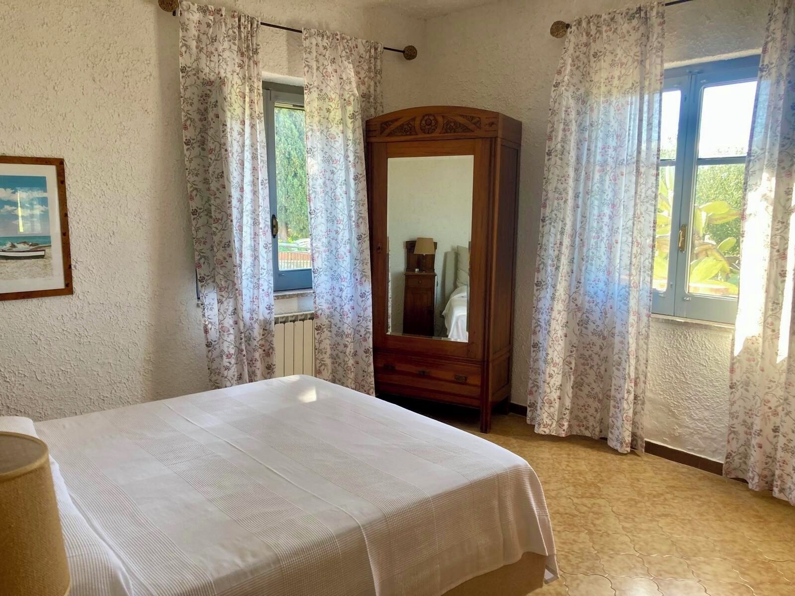 Une chambre à coucher avec un lit, une armoire en bois, une fenêtre avec des rideaux et un radiateur.