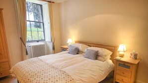 Uma cama bem arrumada com colcha estampada, duas luminárias de cabeceira e uma janela com cortinas.
