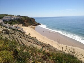 A coastal beach with a rocky cliff and buildings on the left. - 4-STAR LUXURY 2 BED/2 BATH APARTMENT, POOLS, WIFI, AIR-CON, 5 MINS WALK TO BEACH (Burgau)