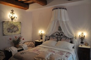 Une chambre à coucher avec un lit à baldaquin, des œuvres d’art florales, des lampes de chevet et une table de chevet avec une horloge.