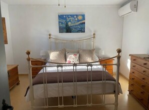 Une chambre à coucher comprenant un lit, des tables de chevet, une commode, un tableau au mur et un appareil de climatisation.