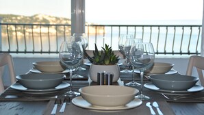 Une table dressée pour un repas, avec des bols, des verres à vin et des couverts, donnant sur une vue sur la côte.