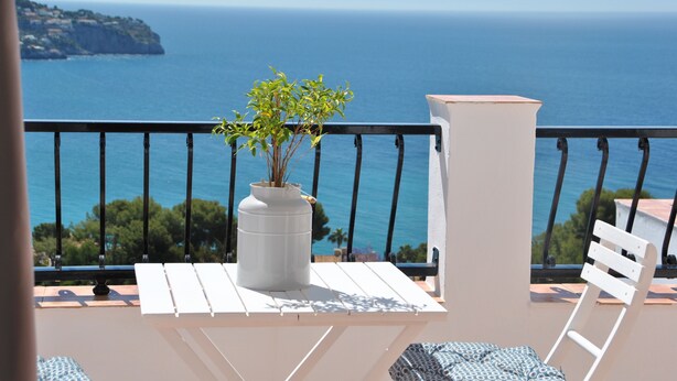 Un balcon avec une table blanche, une plante en pot et une chaise blanche.