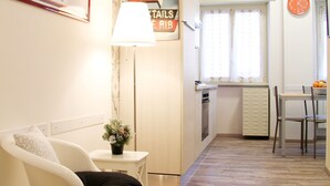 A small, well-lit room with a white chair, a table, and a lamp. There is a window with curtains and a clock on the wall. - Holiday Apartment Maison Velia in San Giovanni Colli Albani Appio Latino district (Roma)