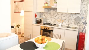 A compact kitchen with white cabinets, a microwave, a stove, and a sink. There is a basket of fruit on the table. - Holiday Apartment Maison Velia in San Giovanni Colli Albani Appio Latino district (Roma)