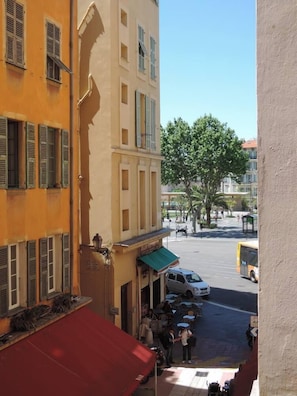 Vista de la calle con un edificio que tiene un toldo rojo y uno verde, una camioneta blanca estacionada en la vía, y un árbol al fondo.