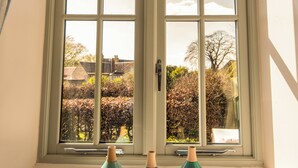 A window with three vases on the sill, curtains with a floral pattern, and a view of a garden and buildings outside. - LUXURY 5* GOLD CONVERTED BARN WITH HOT TUB.TRADITIONAL VILLAGE NORTH OF  LINCOLN (Lincoln)