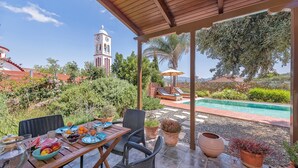 Eine überdachte Terrasse mit Pool, Sitzgelegenheit im Freien und Blick auf einen Kirchturm.