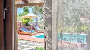Blick durch ein Fenster mit einer Holztür, einem Pool und Sitzgelegenheiten im Freien.